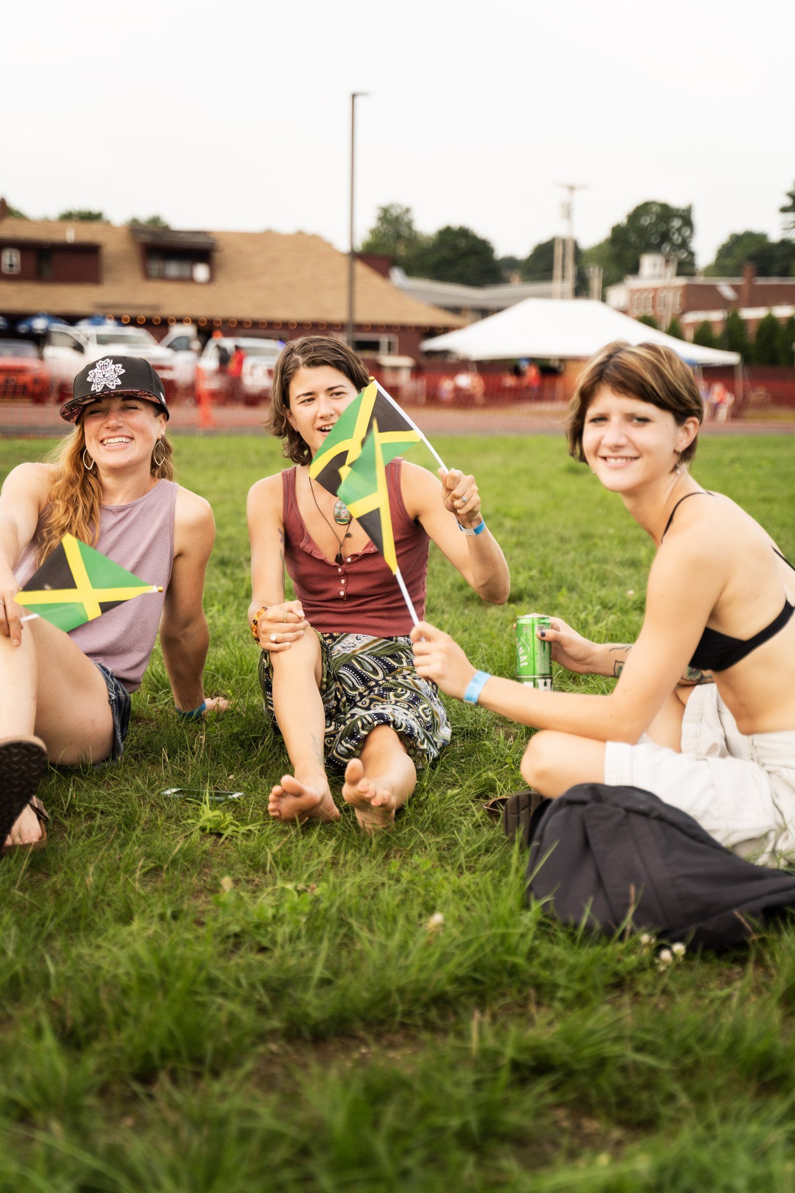 Three friends sitting on the grass waving Jamaican flags, 2024