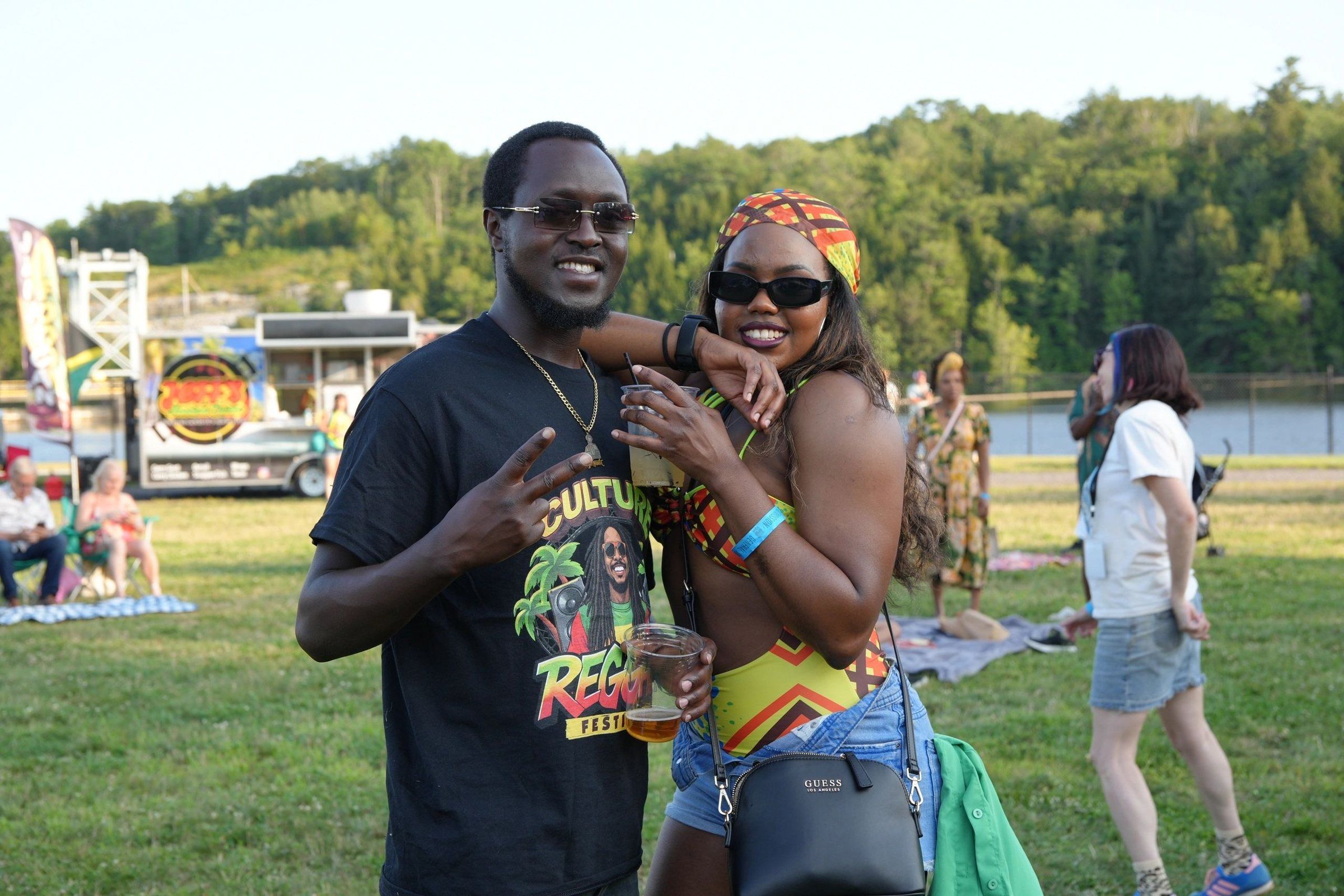 Two friends posing on the lawn, one in a Culture Reggae Festival T-shirt, 2025
