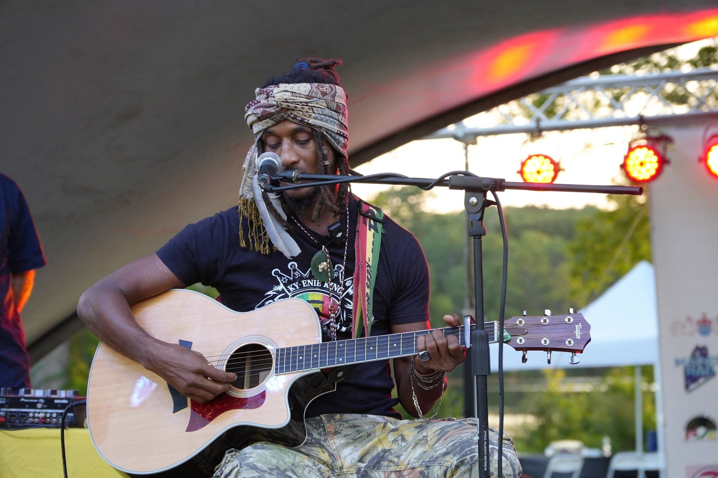 Ky-enie King playing acoustic guitar on the shell stage, 2025